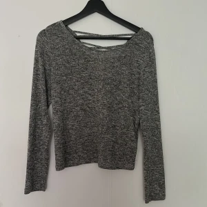 Grå långärmad tröja med öppen rygg från H&M - Säljer en gråmelerad långärmad tröja från H&M. Tröjan har en snygg öppen rygg med banddetalj och är tillverkad i mjukt, stretchigt material. Perfekt för en avslappnad och stilren look.