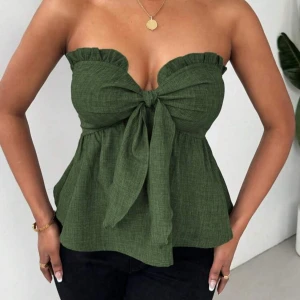 Grön axelbandslös topp med rosett - Säljer den för att den är för liten 💔💔💔💔 HELT NY!!! Snygg grön axelbandslös topp med volangkant upptill och stor rosett framtill. Toppen har en luftig passform och är perfekt för varma dagar. Styla med jeans eller kjol för en trendig look. 