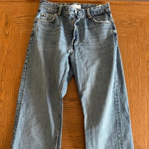 Blå raka jeans från Bershka - Säljer ett par klassiska blå jeans från Bershka med hög midja och raka ben. Jeansen har fem fickor, knapp- och dragkedjegylf samt en enkel, tidlös design. Perfekta för dig som gillar en avslappnad och stilren look.