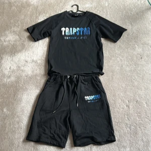 Svarta shortsoch t-shirt från Trapstar med broderad logga - Säljer ett Trapstar summer sett med shorts och t shirt i svart med olika blå nyanser broderat i trapstar loggan helt perfekt för sommaren  och 500 för hela settet (300 kr st)