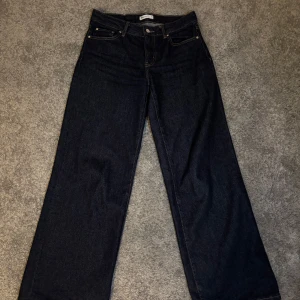 Mörkblå wide jeans från Gina Tricot - Snygga mörkblå jeans från Gina Tricot i modell med raka och vida ben. Klassisk femficksdesign, hög midja och kontrastsömmar. Jeansen är tillverkade i kraftigt denimtyg och passar perfekt till en trendig vardagslook.
