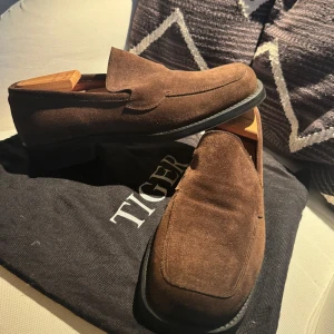 Bruna mockaloafers från Tiger of Sweden - Snygga loafers i brun mocka från Tiger of Sweden. Perfekta för dig som gillar en dressad men avslappnad look. Passar till både jeans och kostym.