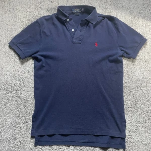 Ralph Lauren pike - Säljer en Ralph Lauren piké mörkblå med rött märke. Den har en liten defekt se bild 4 men man märker det inte när man har den på sig