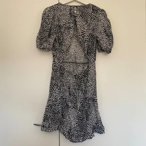 Svart och vit prickig  klänning sommarklänning från NA-KD - Snygg svart och vit  klänning från NA-KD med korta ärmar och ett prickigt mönster. Klänningen har en öppen rygg. Den är gjord i ett lätt och luftigt material.