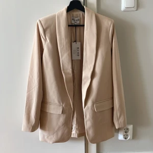 Oanvänd beige blazer från NA-KD - Säljer denna fina oanvända blazer från NA-KD i storlek 36 pga beställde fel storlek. Den är axelvadderad. Köparen står för eventuell frakt. Kan mötas upp i Uppsala