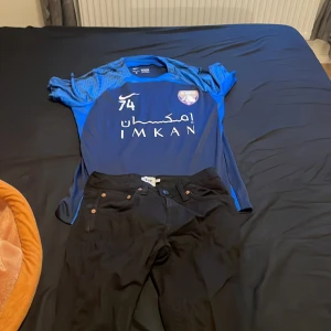 Blå fotbollströja från Nike - Säljer en blå fotbollströja från Nike med korta ärmar och tryck på framsidan. Perfekt för fotbollsfans som vill visa sitt stöd. Tröjan har en sportig design med klubbmärke och sponsorlogga. Och jenas T-shirt kommer Ålltsa me jeans  bra för sommaren bra stil 