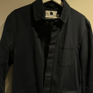 Blå overshirt  med knappar NN07 - Snygg svart kappa med knappar framtill och en bröstficka. Perfekt för en stilren look. Passar bra till både vardag och mer uppklädda tillfällen.