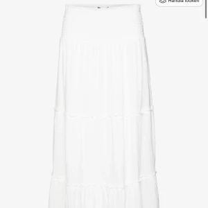 Vit långkjol med volanger - Säljer en vacker vit långkjol med volanger. Kjolen har en smockad midja som ger en bekväm passform och ett luftigt fall. Perfekt för varma dagar eller sommarens fester. 🌸man kan ha den både låg och högmidjad beroende på hur man vill ha den:) storlek L men är mer som en M