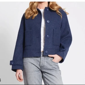 Blå ulljacka - Snygg blå ulljacka med knappar framtill och stora fickor. Jackan har en kortare, fin passform och långa ärmar med knappdetaljer vid ärmsluten. Perfekt för kyligare dagar!