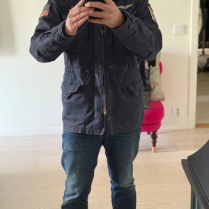 The Iconic Field Jacket Polo Ralph Lauren NAVY - Ralph Lauren jacka storlek s men fits S-M. Grym  skick, knappt använd. nypris ligger runt 5k och  är svår att få tag på.                                                  Säljer en navy blue militärinspirerad jacka från Ralph Lauren med flera patchar, inklusive en amerikansk flagga och en flygdivisionsemblem. Jackan har dragkedja och knappar framtill samt flera fickor för praktisk förvaring. Perfekt för en cool och avslappnad stil. Passar Medium också. Svår att få tag på. 