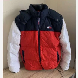 Dunjacka från Tommy Hilfiger - Snygg pufferjacka i rött, vitt och blått från Tommy Hilfiger. Jackan har en dragkedja framtill och en hög krage för extra värme. Perfekt för kyliga dagar med sin vadderade design och praktiska fickor. Men kan användas under våren och hösten jackan är bara använd en vinter 1 vecka typ men tyckte inte om den så vill sälja den. Prisen kan diskuteras vid snabb affär 