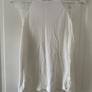Vit spets topp från Zara - Säljer en stilren vit spets topp från Zara med vackra spetsdetaljer vid axlarna. Perfekt för en elegant look. Tillverkad i Portugal. Passar bra till både jeans och kjol.