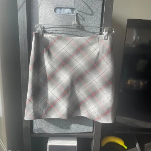 Grå rutig kjol från Esprit - Snygg grå kortkjol från Esprit med ett klassiskt rutigt mönster i rött och svart. Perfekt för en stilren look. Kjolen har en enkel och elegant design som passar till många olika tillfällen.