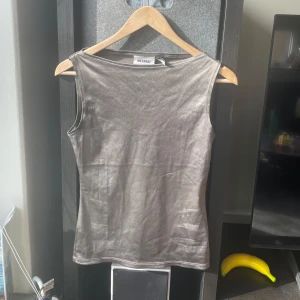 Grå ärmlös topp från Weekday - Snygg grå ärmlös topp från Weekday i ett glansigt material. Perfekt för en stilren look. Toppen har en enkel design som gör den lätt att matcha med olika outfits.