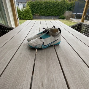 Vita och turkosa fotbollsskor från Nike - Säljer ett par vita och turkosa fotbollsskor från Nike med en unik design och turkosa sulor. Skorna har en modern look med svarta detaljer och är perfekta för fotbollsplanen. De har en stilren och funktionell design som ger bra grepp och komfort.