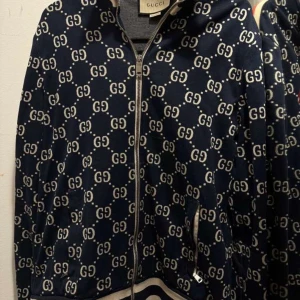 Mönstrad jacka från Gucci - Säljer min väns snygga blå  tröja från Gucci med det ikoniska GG-mönstret. Jackan har dragkedja och långa ärmar. Tillverkad i Italien med högkvalitativt material. Perfekt för dig som vill ha en stilren och lyxig look.