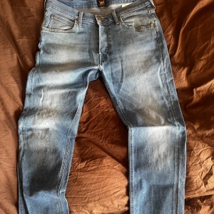 Blå jeans från Lee - Snygga blå jeans från Lee med klassisk femficksdesign och knappgylf. De har en normal/slim passform och är perfekta för sommaren. Bra skick och riktigt snygg tvätt. W31 L32. Kööööööp!