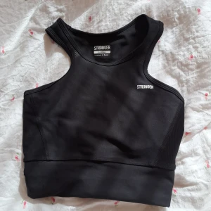 Svart linnetopp från Stronger - Säljer en svart linnetopp från Stronger. Toppen har en sportig design med breda axelband och rund halsringning. Perfekt för träning eller en aktiv vardag.