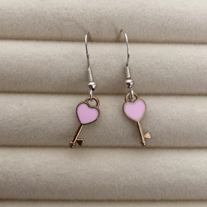 Rosa hjärtformade nyckelörhängen - Charmiga örhängen i form av nycklar med hjärtformade toppar i rosa. Perfekta som en söt accessoar för att ge en lekfull touch till din stil.