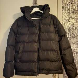 Svart pufferjacka med huva - Säljer en svart pufferjacka med huva och dragkedja. Jackan är perfekt för kalla dagar och har en bekväm passform. Den är långärmad och har en stilren design💕