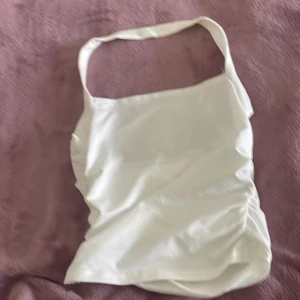 Vit ärmlös topp - Säljer en stilren vit ärmlös topp med rynkade detaljer på sidan. Perfekt för en somrig look. Toppen har en enkel design med smala axelband.