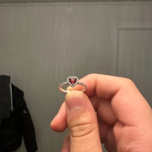PANDORA Silverring med hjärtformad röd sten - Elegant silverring med en hjärtformad röd sten i mitten, omgiven av små glittrande stenar. Perfekt för att ge en romantisk touch till din stil.