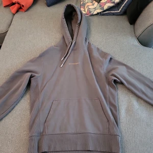 Grå grön hoodie från Superdry - Säljer en stilren grå grön hoodie från Superdry med justerbar huva och känguruficka. Perfekt för en avslappnad look. Superdry-loggan är tryckt på bröstet. Ganska stor i storleken!