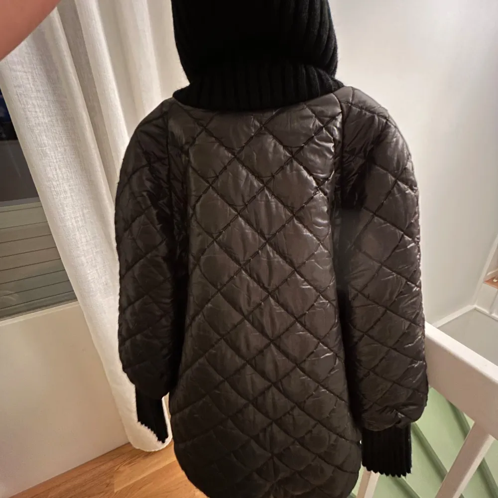 Snygg svart quiltad jacka med dragkedja och knappar. Jackan har en hög ribbad krage och långa ärmar med ribbade muddar. Perfekt för kyligare dagar.. Takit.