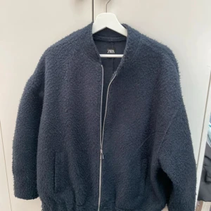 Mörkblå teddyjacka från Zara - Säljer en mysig mörkblå teddyjacka från Zara. Jackan har en dragkedja framtill och är långärmad med en bekväm passform. Perfekt för kyliga dagar när du vill hålla dig varm och stilren.