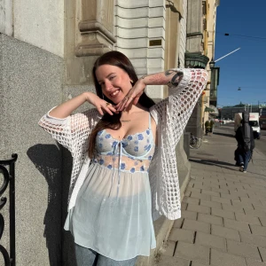 Blå blommig mesh top - Söt blå meshtop med blommor. Den har smala axelband och en rosett framtill, bh knäppe bak. Endast använd 1 gång på en konsert