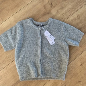 Grå kofta från Gina Tricot - Säljer en mysig grå trekvartsärmad kofta från Gina Tricot med knappar framtill. Helt oanvänd med prislapp, nypris 400kr. Säljer då jag är en guldtjej och knapparna är silver❤️