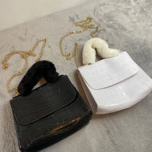 Svart och vit axelväska med pälsdetalj - Två eleganta axelväskor i svart och vit med krokodilmönster och guldkedja. Väskorna har en mjuk pälsdetalj på handtaget som ger en lyxig känsla. Perfekt för att lyfta din outfit med en touch av glamour.