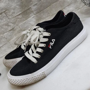 Svarta sneakers från Fila - Snygga svarta sneakers från Fila med vit sula och klassisk snörning. Skorna har en broderad Fila-logga på sidan och en slitstark gummisula. Perfekta för en avslappnad stil.