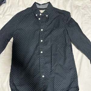 Svart prickig skjorta - Snygg svart skjorta med vita prickar och klassisk krage. Skjortan har långa ärmar och knappar framtill. Perfekt för en stilren look.