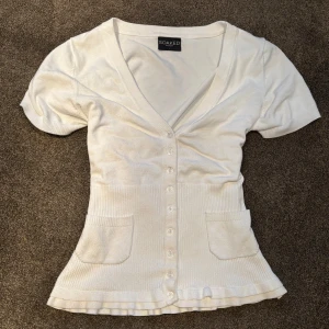 Vit kortärmad kofta  - Säljer en vit kofta från Soaked med korta ärmar och v-ringning. Koftan har knappar framtill och två fickor. Storlek L men extremt liten i storlek och passar mig som vanligtvis har XS/S.