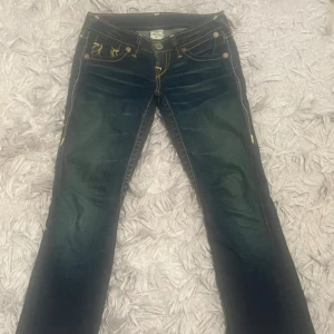 True religion jeans! - Snygga mörkblå jeans från true religion storlek 26 med unika broderade detaljer i gult på bakfickorna. Jeansen har en klassisk femficksdesign och knappar framtill.på första bilden kan man se en liten skada på jeansen vid låret men inget man märker.