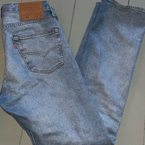 Levis 501 ljusblå jeans - Säljer ett par klassiska Levis 501 jeans i ljusblå denim. De har en rak passform och är tillverkade i bomull. Perfekta för en avslappnad stil. Jeansens ikoniska design gör dem tidlösa och mångsidiga.