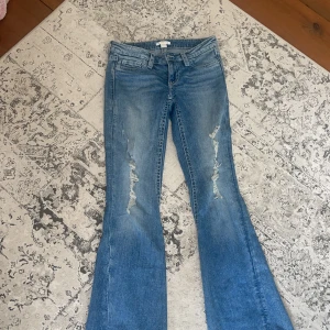 Blå bootcut jeans från Gina Tricot - Snygga blå bootcut jeans från Gina Tricot i storlek S. Jeansen har slitna detaljer framtill, klassiska bakfickor med dekorativa sömmar och knappar. Modellen har låg midja och är tillverkad i mjukt denimtyg med lite stretch.