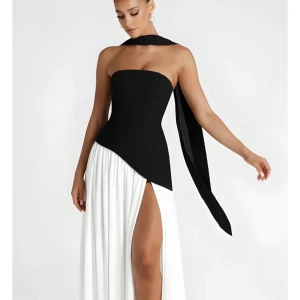 Svartvit långklänning med slits - Supersnygg svartvit långklänning med asymmetrisk överdel och hög slits. Klänningen är axelbandslös och har en cool scarf-detalj runt halsen. Kjolen är vit och flowy medan överdelen är svart och figurnära. Perfekt för dig som vill sticka ut! Finns i storlek L, m