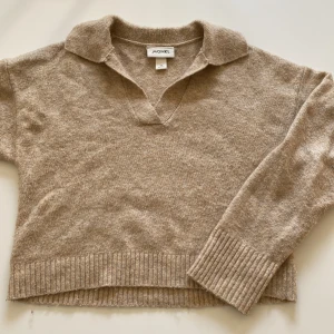 Beige stickad tröja med krage från Monki - Beige stickad tröja från Monki i storlek XS. Tröjan har en klassisk krage och v-ringning, samt ribbade muddar vid ärmslut och nederkant. Perfekt för lager-på-lager.