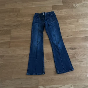 Blå bootcut jeans från Gina Tricot - Snygga blå bootcut jeans från Gina Tricot med markerade sömmar framtill och stora fickor. Jeansen har låg midja och klassisk denimlook, perfekta för en trendig vardagsstil.