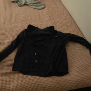 Mörkblå skjorta från GANT 158/164 - Snygg mörkblå skjorta från GANT med klassisk krage och knappar framtill. Skjortan har lång ärm och broderad GANT-logga på bröstet. Perfekt för dig som gillar stilrena och tidlösa plagg.