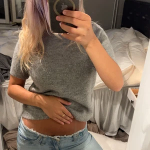 Grå stickad kortärmad tröja - Mysig grå stickad tröja med korta ärmar och rund hals. Tröjan har en lite croppad passform och är perfekt att styla med jeans. Enkel och stilren design som funkar året runt.