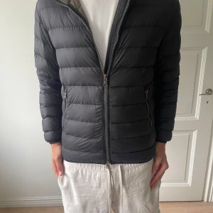 Svart dunjacka från Colmar med huva - Säljer en svart dunjacka från Colmar med huva och horisontella sömmar. Jackan har dragkedja framtill, två fickor med dragkedja och en snygg logga på ärmen. Perfekt för kyliga dagar och riktigt skön att bära.