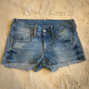 Lågmidjade jeansshorts - Super snygga blå jeansshorts från G-Star RAW med slitna detaljer. Klassisk femficksmodell med låg midja och cool tvättad look. Midjemåttet rakt över är ca 37 cm men shortsen är i ett stretchigt material💕