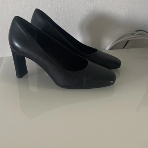 Svarta klassiska pumps med klack - Stilrena svarta pumps med lagom klack och rundad tå. Skorna har en minimalistisk design och är tillverkade i slätt material som ger en elegant look. Perfekta för dig som gillar en tidlös och clean stil