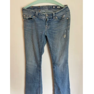 Ljusblå Miss Me jeans med broderi - Snygga ljusblå jeans från Miss Me med bootcut passform. Jeansen har slitna detaljer framtill och bakfickor med stora broderade mönster och paljetter. Klassisk femficksmodell med silverfärgade nitar och dekorativa sömmar. Perfekta för dig som gillar statement-jeans. Lagning vid skrevet men färgen på lagningen passar in