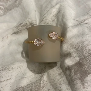 Guldarmband Caroline Svedbom med rosa kristaller - Snyggt armband i guldton från Caroline Svedbom med tvinnad design och två stora, ljusrosa kristaller i droppform. Perfekt statement piece, som lyfter vilken outfit som helst. 💕✨
