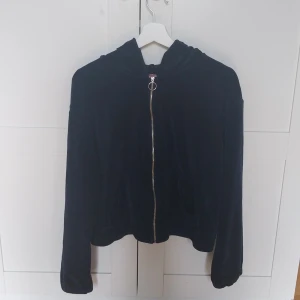 Marinblå velourkofta från Hunkemöller - Mysig marinblå velourkofta från Hunkemöller med huva och dragkedja framtill. Tröjan har långa ärmar, elastisk nederkant och en enkel, clean look. Perfekt för chill dagar eller när du vill ha något bekvämt och snyggt att slänga på dig. Koftan har dock en skadad ärm men det är inget som syns. Storleken är L men jag har använt den  och jag har XS/S. Så den funkar som det oxå.