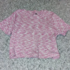 Rosa och vit kortärmad stickad tröja - Superfin kortärmad stickad tröja i rosa och vitt mönster. Tröjan har en avslappnad passform och är perfekt för dig som gillar en söt och chill stil. Mjuk och skön, passar perfekt till jeans eller kjol.